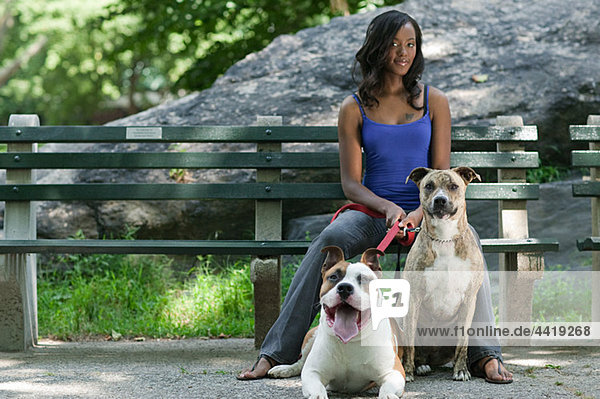 Frau mit ihren beiden Hunden auf der Parkbank sitzend