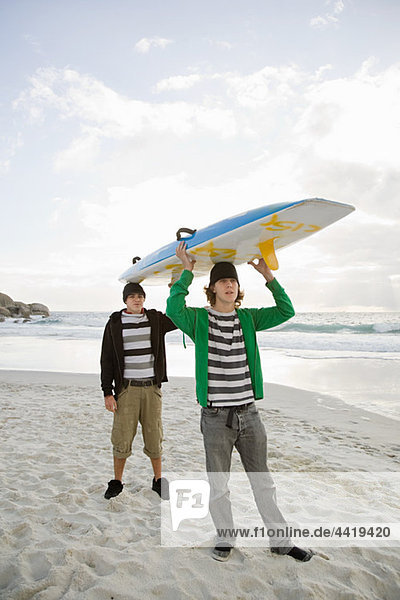 Young men carrying surfboard on head