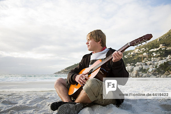 Junger Mann spielt Gitarre am Strand