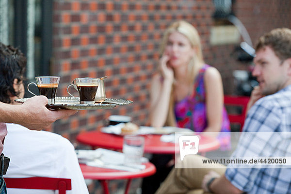 Kellner mit Kaffee für Leute außerhalb des Cafés
