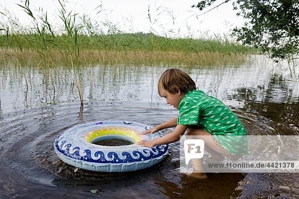 Junge spielt mit Schlauch am Rand des Sees