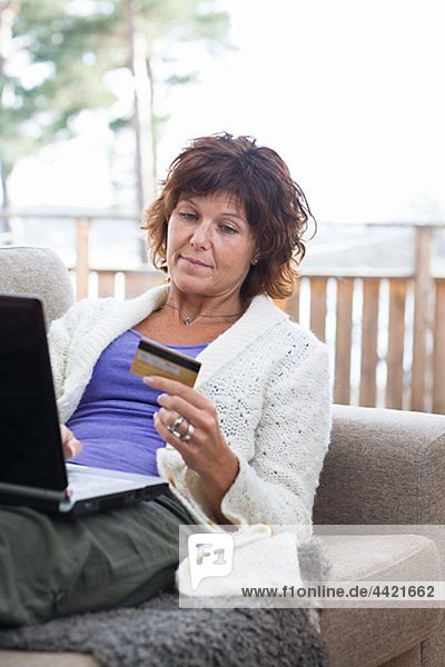 Woman sitting with laptop holding credit card