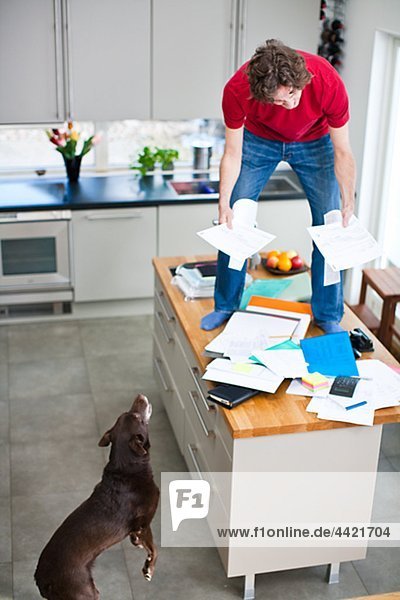 Man struggling with domestic paperwork while dog is watching