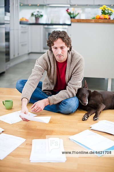 Mid-adult man arranging domestic paperwork on floor  while dog is sleeping next to him
