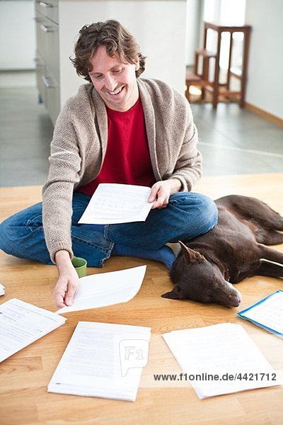 Mid-adult man arranging domestic paperwork on floor,  while dog is sleeping next to him