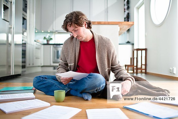 Mid-adult man doing paperwork on floor,  while dog is sleeping next to him