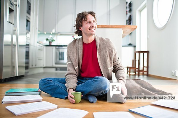 Mid-adult man doing paperwork on floor,  while dog is sleeping next to him