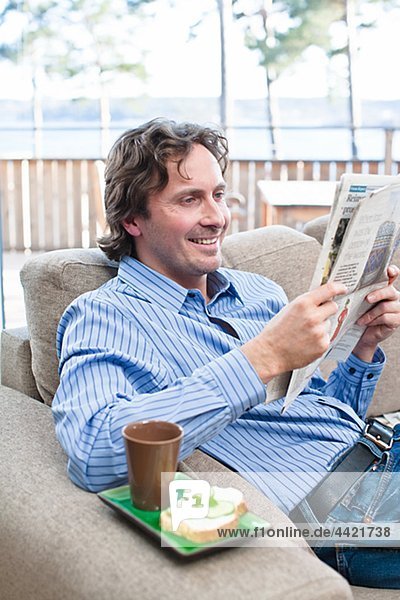 Mid-adult man sitting on sofa  reading newspaper