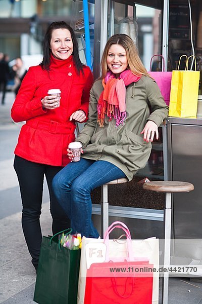 Pair of young women taking break from shopping  drinking takeaway coffee