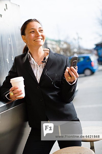Fröhlich geschäftsfrau mit Takeaway Kaffee in einer Hand und Handy in einem anderen