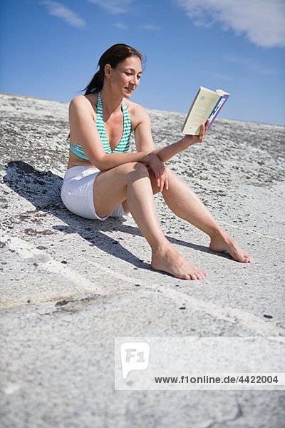Woman sitting on rock and reading book  smiling