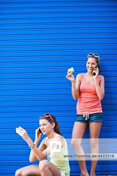 Zwei Girls vor der blauen Wand  sprechen auf Handys