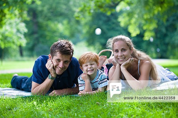 Parents with son lying in park and looking at camera
