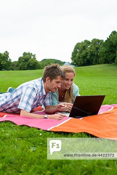 Mid adult couple lying on blanket and using laptop