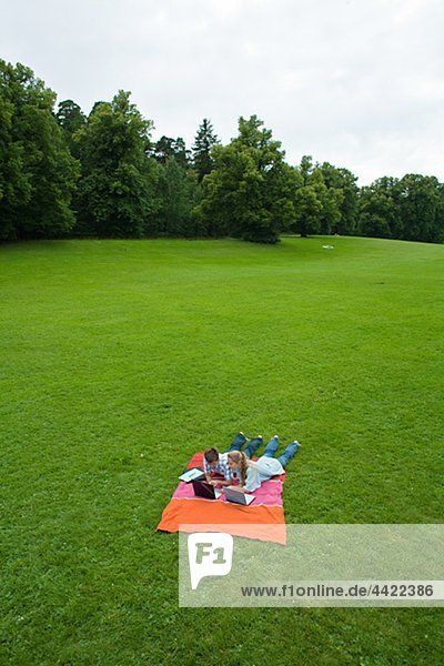 Couple with laptops lying on blanket in park