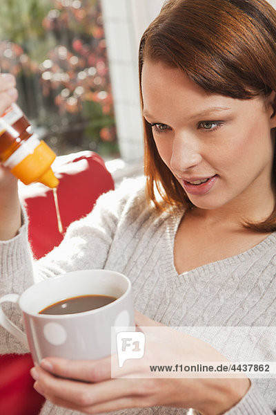 Young woman pouring honey into her tea cup