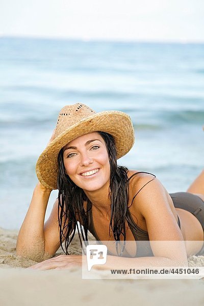 Portrait of a beautiful brunette woman smiling at camera with a hat at the beach