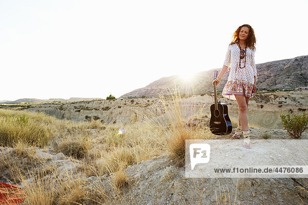 Woman carrying guitar at sunset