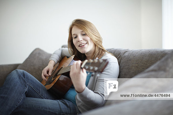 Mädchen sitzt auf dem Sofa und spielt Gitarre.