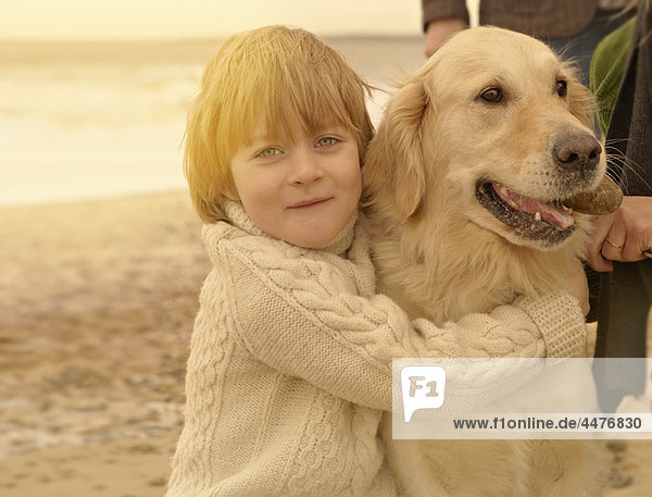 Kleiner Junge  der den Hund umarmt. Strand