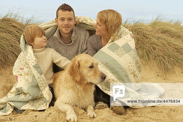 Familie mit Hund  unter Bettdecke  am Strand
