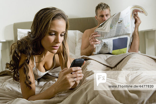 Junge Frau mit Smartphone im Bett
