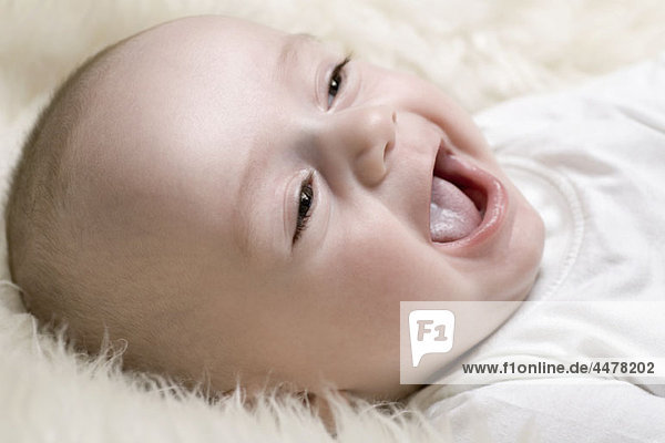 Ein fröhliches Baby liegt auf einem Flickenteppich