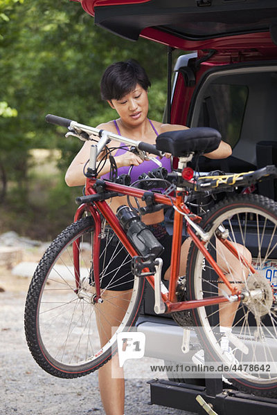 Eine Frau  die ein Fahrrad von einem Fahrradträger auf ihrem SUV nimmt.
