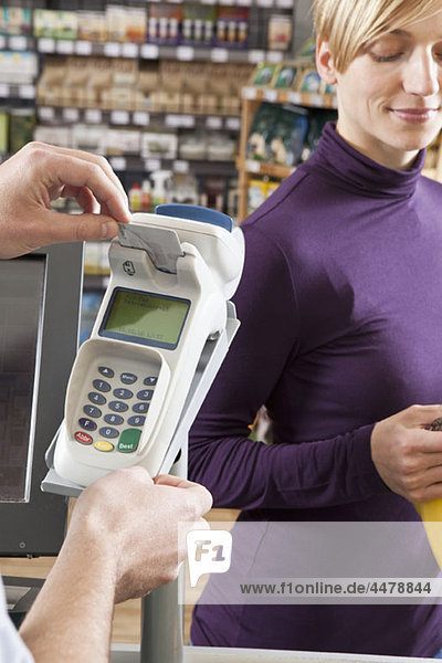 Ein Kassierer  der eine Karte in einen Kreditkartenautomaten im Supermarkt steckt.