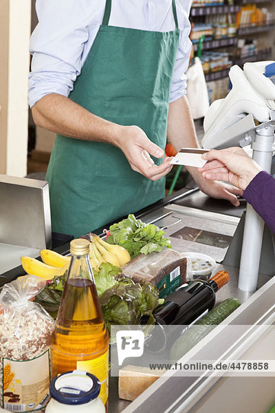 Ein Kunde  der einer Kassiererin eine Kreditkarte im Supermarkt übergibt.