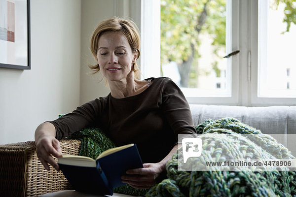 Eine Frau liest ein Buch  während sie auf dem Sofa liegt.