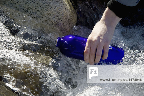 Detail einer Person  die eine Trinkflasche in einem Fluss füllt.