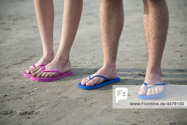 A young couple wearing flip-flops at the beach  low section