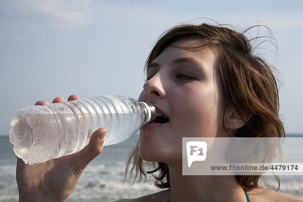 Eine Frau die Wasser in Flaschen am Strand trinkt.