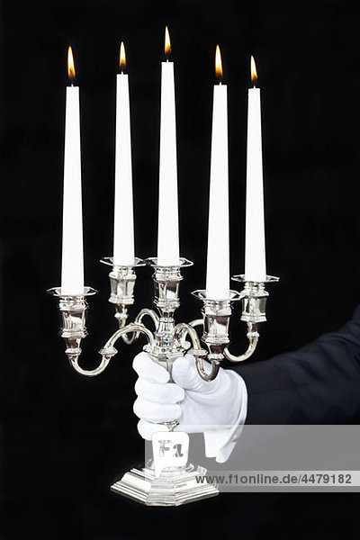 Ein Butler hält einen Kandelaber mit angezündeten Kerzen  Fokus auf die Hand.