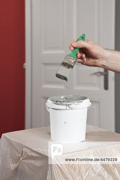 A man dipping a paintbrush into a paint can  focus on hand