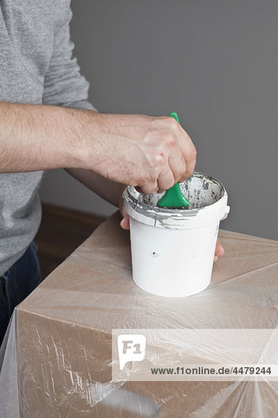 A man dipping a paintbrush into a paint can  focus on midsection  hand