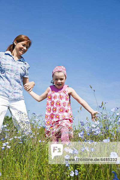 Mutter und Tochter laufen über eine Blumenwiese