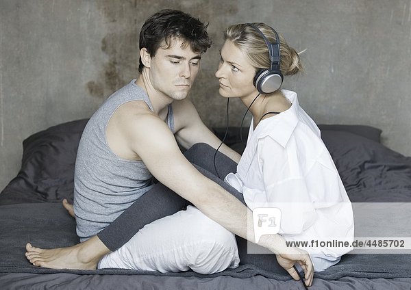 Young couple sitting on bed with headphones