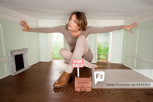 Junge Frau in kleinem Haus mit Hausmodell zu verkaufen