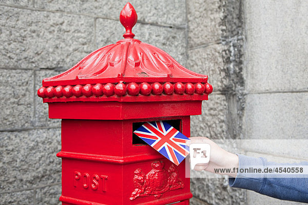 Person putting postcard in post box  London