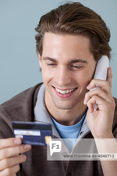 Junger Mann am Telefon mit Kreditkarte