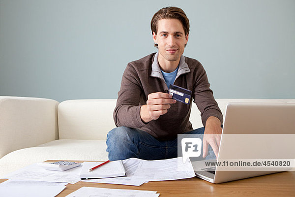 Junger Mann mit Kreditkarte mit Laptop