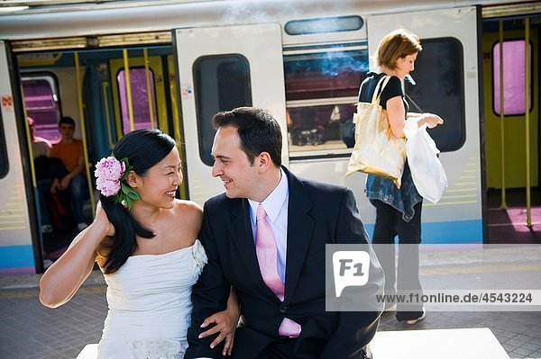 Happy multi-ethnic bride and groom looking at each other in train station
