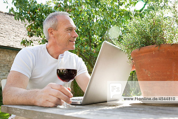 Senior Mann mit Laptop und Rotwein