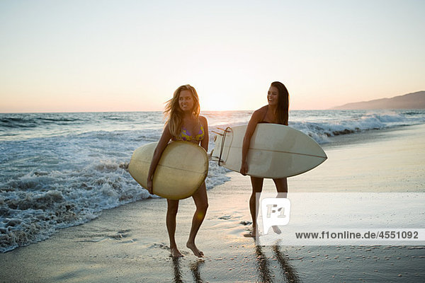 Female surfers by the sea at sunset