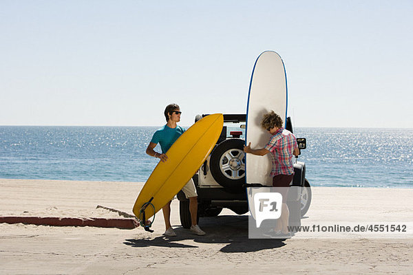 Two young men by SUV with surfboards