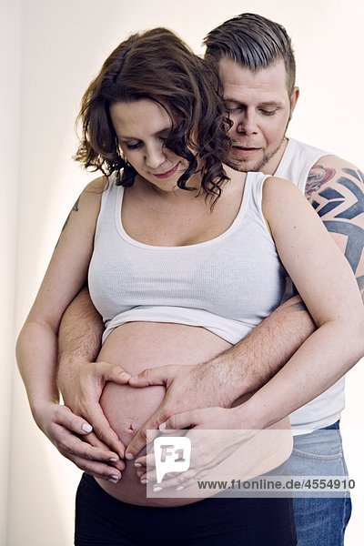 Mann bilden Herz-Form mit Händen auf schwangere Frauen Bauch