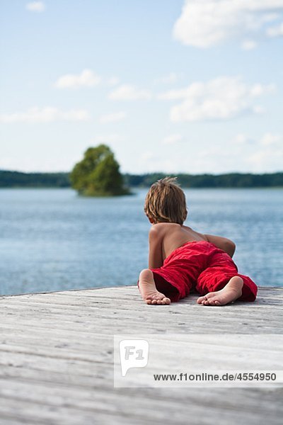 Boy lying on pier and looking at lake