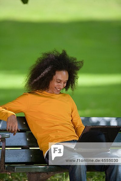 Smiling young man with afro hair sitting on bench with laptop